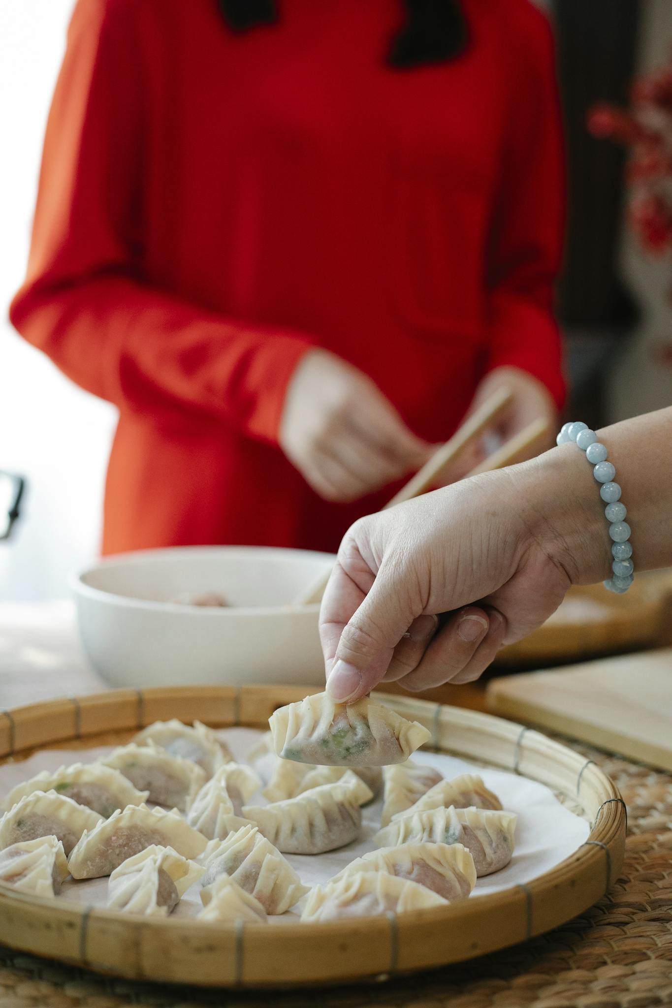 Crop anonymous women preparing traditional Chinese jiaozi dumplings while standing at table in kitchen in daylight